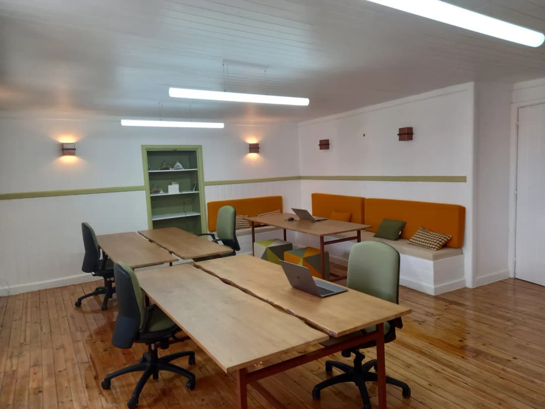 Shared coworking room with long wooden desks, office chairs, a laptop and bench seating