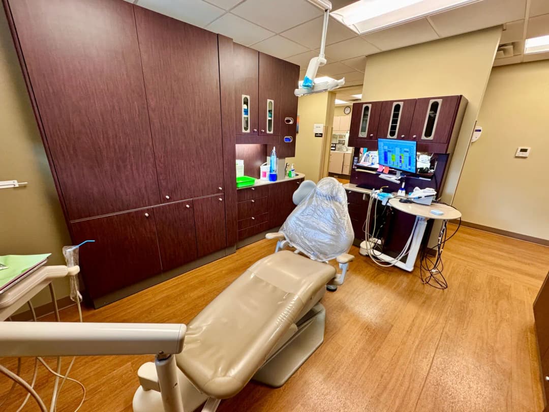 Empty dental treatment room with a patient chair, overhead light and dentist monitor
