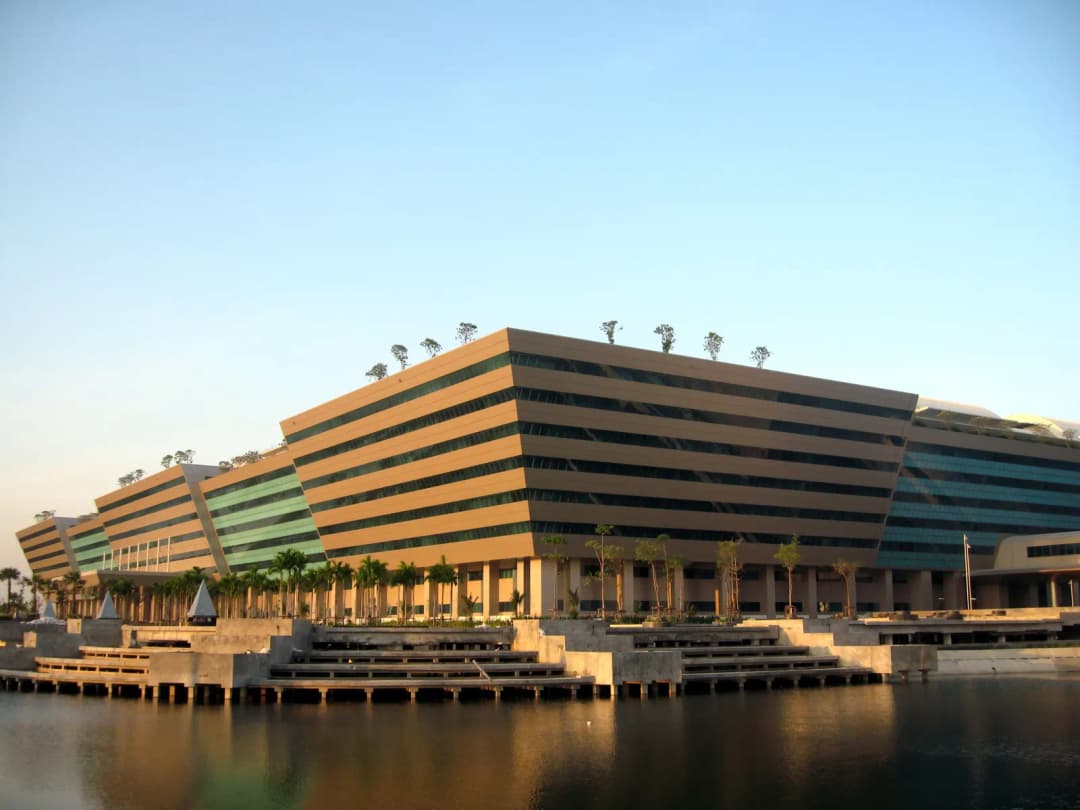 Government Complex building on Chaeng Watthana Road in Bangkok at sunset, behind a reflecting pond